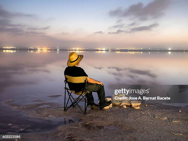 relaxed person sat in a chair opposite to a lake looking at the putting sun - alicante street stock pictures, royalty-free photos & images