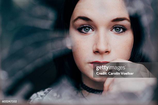 young woman with dark hair and pale skin looking through broken glass - pale complexion stock-fotos und bilder