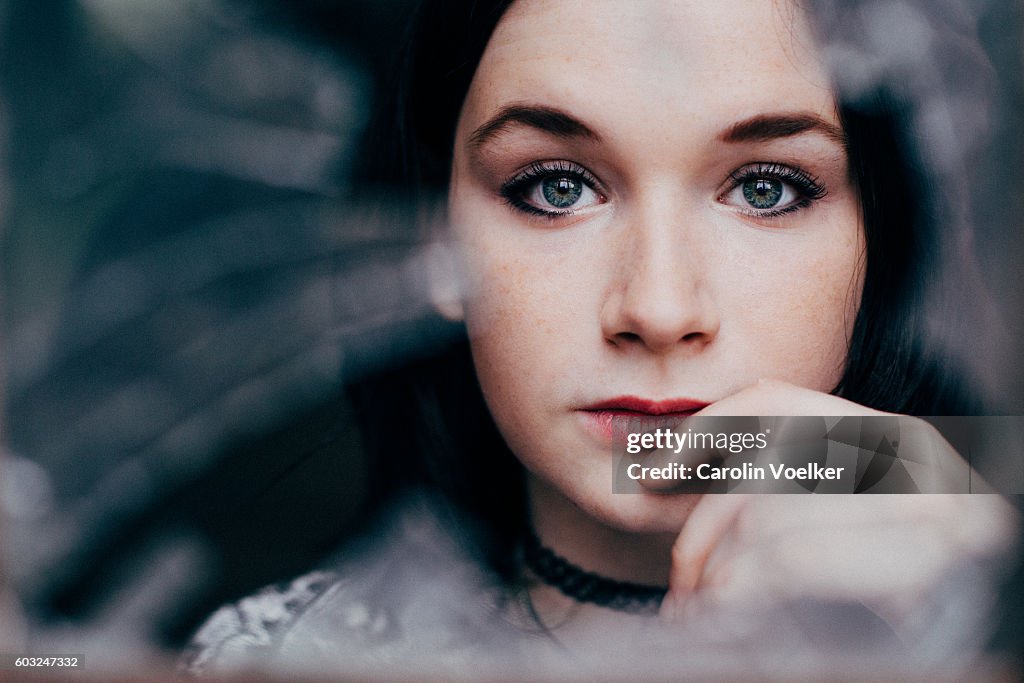 Young woman with dark hair and pale skin looking through broken glass