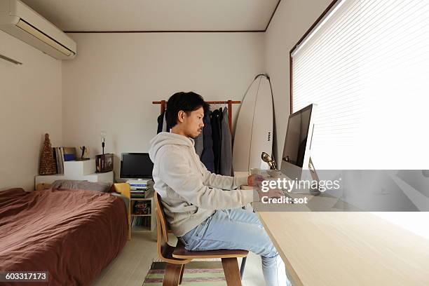 young man using computer at desk - junggeselle stock-fotos und bilder