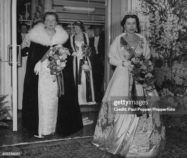 Queen Elizabeth II of Great Britain and Queen Juliana of the Netherlands both wearing evening gowns and tiaras, carry bouquets as they leave the...