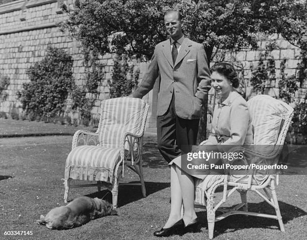 Queen Elizabeth II and Prince Philip, Duke of Edinburgh pictured sitting on lawn chairs with the Queen's corgi 'Sugar' below the East Terrace of the...
