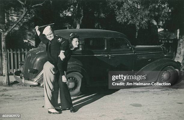 Sailor pretends to spank girlfriend. Car in background