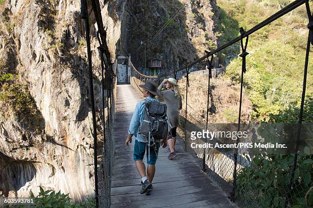 hiking couple walk across suspension bridge - hängebrücke stock-fotos und bilder