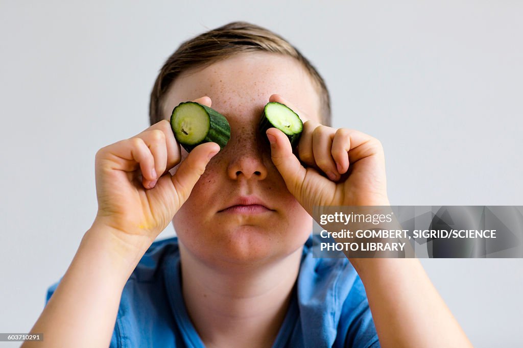 Boy holding cucumber over eyes