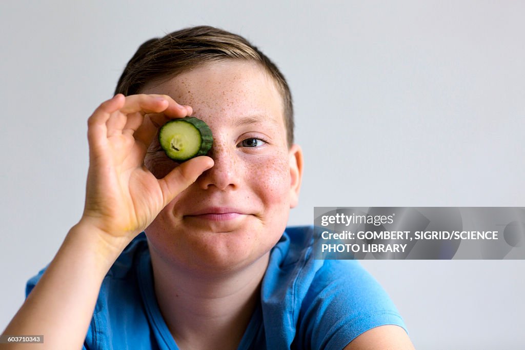 Boy holding cucumber over eye