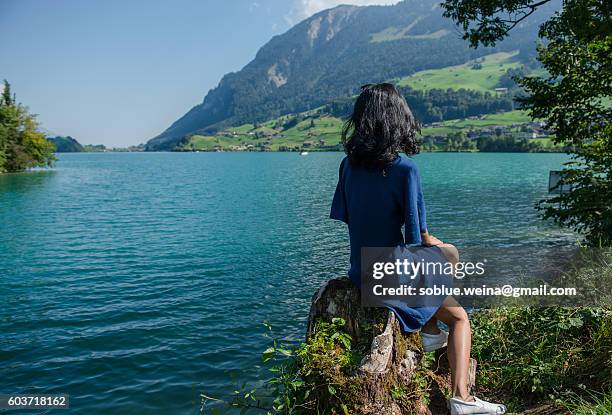 an asian woman in blue dress is sitting by lake lungern enjoying the view of lungernsee and the swiss alps on a summer day - lungern switzerland stock-fotos und bilder