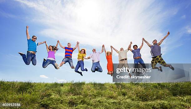 gente alegre cogida de la mano y saltando en lo alto contra el cielo. - salto alto fotografías e imágenes de stock