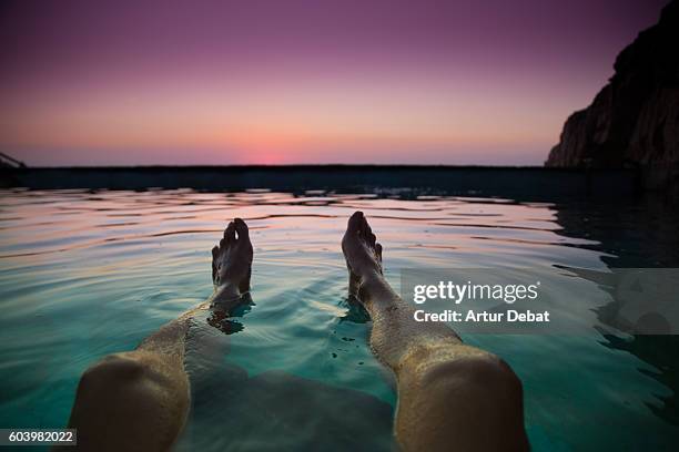 guy from personal perspective swimming in a natural pool in the mediterranean sea costa brava shoreline watching the sunrise with his feet floating into the water during summer time. - legs in water fotografías e imágenes de stock