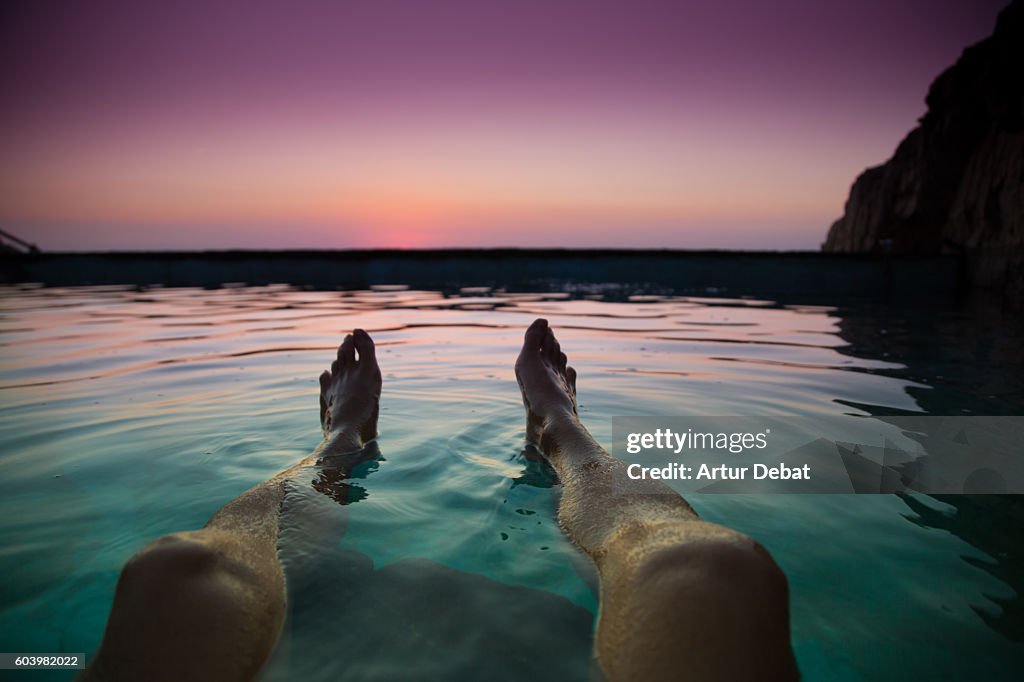 Guy from personal perspective swimming in a natural pool in the Mediterranean Sea Costa Brava shoreline watching the sunrise with his feet floating into the water during summer time.