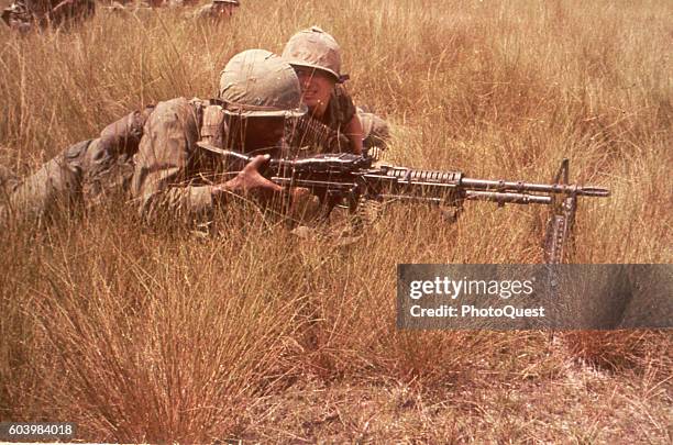 American soldiers of the 1st Infantry Division lie in tall grass with an M60 machine gun, Bien Hoa, Vietnam, October 1965.