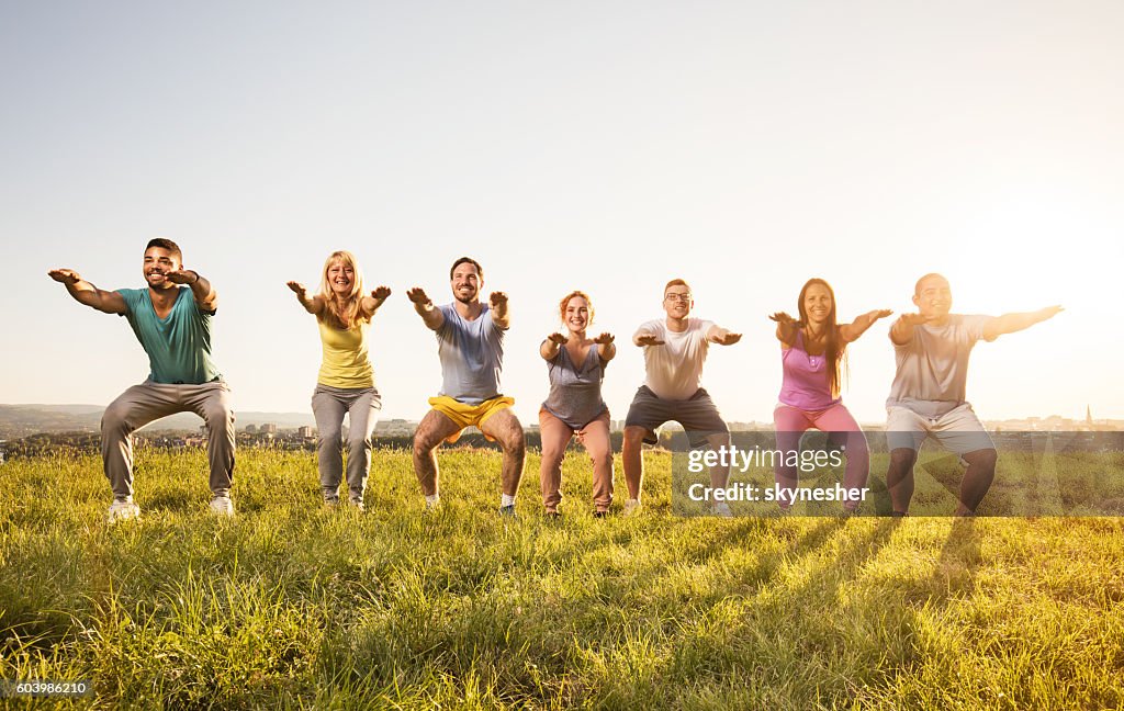 Lächelnde Gruppe von Menschen, die Kniebeugen machen und in der Natur trainieren.