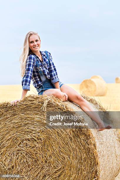 young blonde sitting on bale of straw on field - josef mohyla stock pictures, royalty-free photos & images