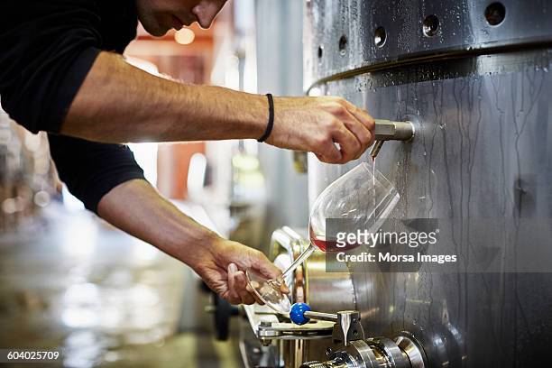 man filling wine from storage tank in winery - destilería fotografías e imágenes de stock
