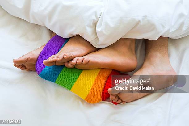 two mens feet on a rainbow hot water bottle - feet in bed stock-fotos und bilder