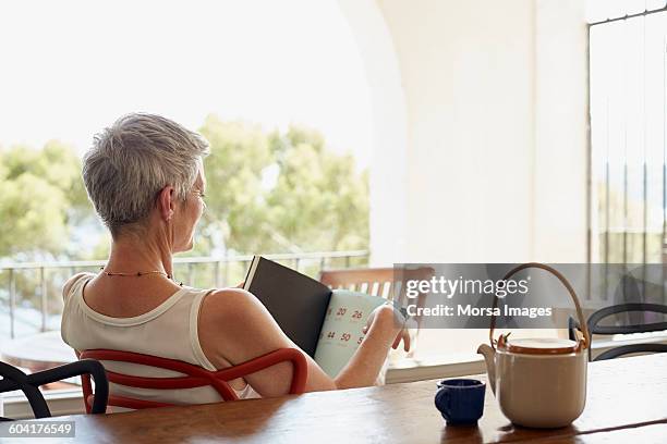 senior woman holding book while siting on chair - grey hair back stock pictures, royalty-free photos & images