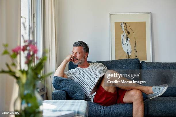 thoughtful man looking away while relaxing on sofa - benen over elkaar geslagen stockfoto's en -beelden