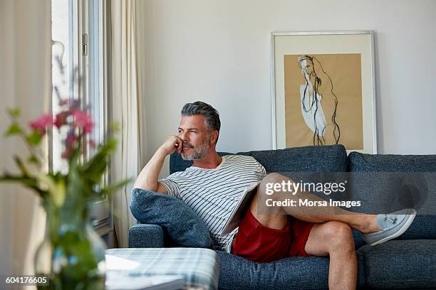 thoughtful man looking away while relaxing on sofa - cross legged stock pictures, royalty-free photos & images