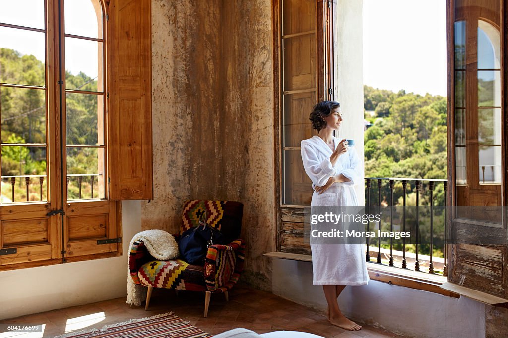 Woman having coffee while standing at window