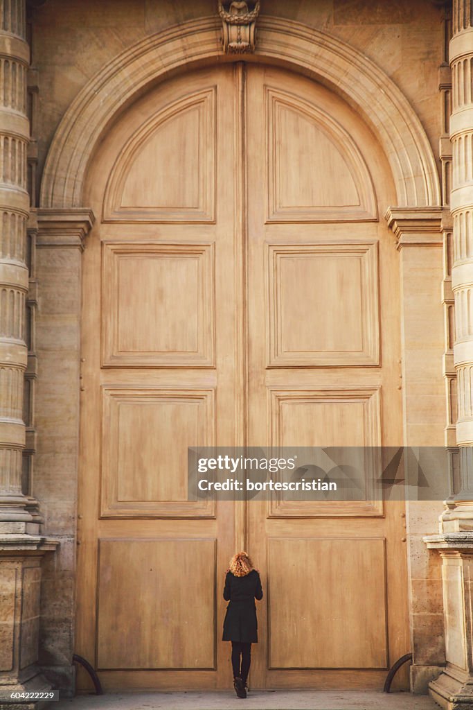 Rear View Of Woman Standing Against Closed Wooden Door Of Historic Building