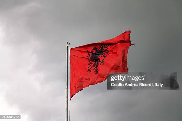 flag of albania against a dramatic sky - albania fotografías e imágenes de stock