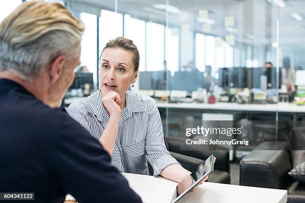 geschäftsfrau zeigt auf tablet und erklärt männlichen kollegen - business meeting table stock-fotos und bilder