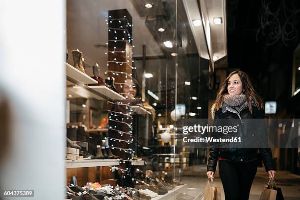 spain, reus, smiling young woman looking at window display in the evening - reus spain stock pictures, royalty-free photos & images