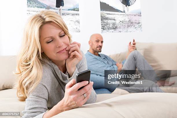 mature couple sitting on sofa using their smart phones - neid stock-fotos und bilder