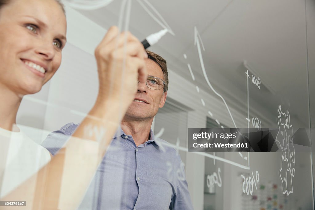 Young woman writing onto glass wall in office