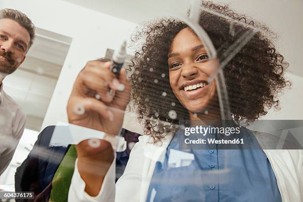 young woman writing onto glass wall in office - facial expression girl office stock-fotos und bilder