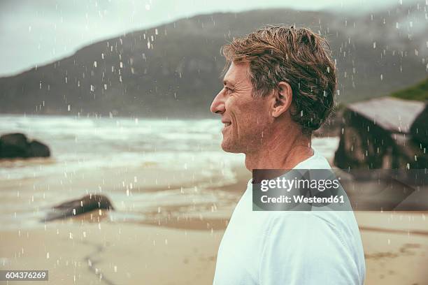 brazil, florianopolis, profile of happy man standing in the rain on the beach - people rain happy stockfoto's en -beelden