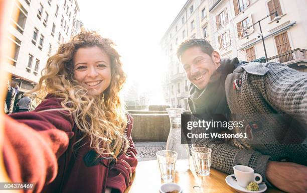 italy, milan, couple sitting at sidewalk cafe taking selfies - milan cafe stock pictures, royalty-free photos & images