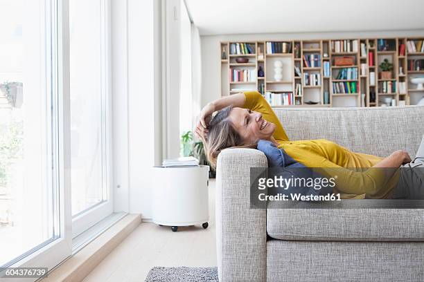 happy woman at home lying on couch - mature women laughing stock pictures, royalty-free photos & images