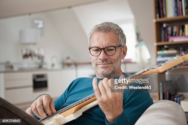 mature man at home playing guitar - freizeitaktivität stock-fotos und bilder