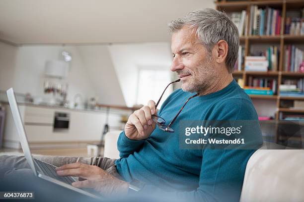 mature man at home sitting on couch using laptop - laptop sleeve stock pictures, royalty-free photos & images