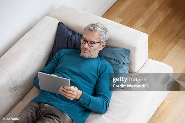 mature man at home lying on couch using digital tablet - cushion top view stock pictures, royalty-free photos & images