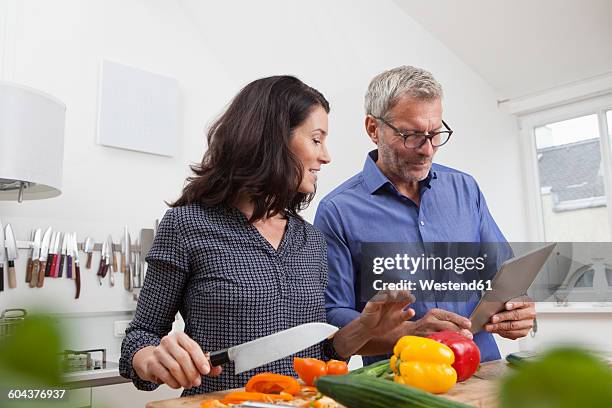 mature couple with digital tablet cooking in kitchen - middle aged couple cooking ストックフォトと画像