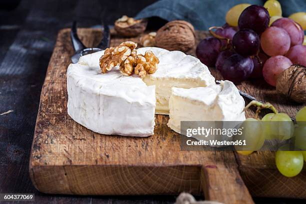 wooden board with sliced camembert, walnuts and grapes - camembert stock-fotos und bilder