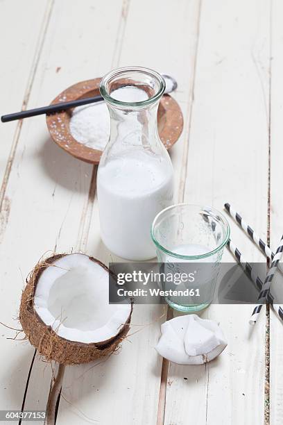 opened coconut, glass and carafe of homemade coconut milk and coconut flakes - rietje los stockfoto's en -beelden