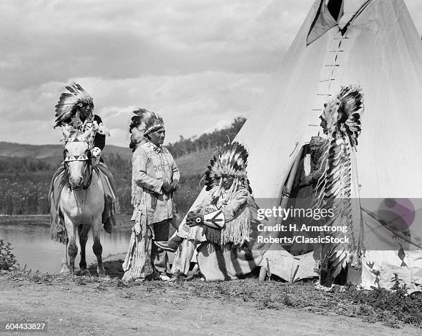 1920s FOUR NATIVE AMERICAN STONEY SIOUX INDIAN MEN ASSEMBLED BESIDE TEPEE WEARING FULL EAGLE FEATHER WAR BONNETS ALBERTA CANADA