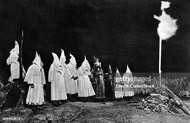 1930s KU KLUX KLAN GATHERING WITH IMPERIAL WIZARD OPPOSITE BURNING CROSS IN RURAL GEORGIA USA