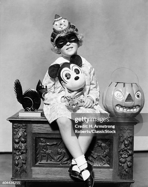 1930s LITTLE GIRL HOLDING MICKEY MOUSE TOY WEARING MASK CLOWN HAT LOOKING AT CAMERA SITTING BESIDE BLACK CAT HALLOWEEN PUMPKIN