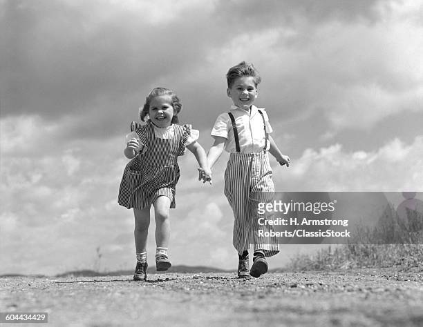 1940s BOY GIRL HOLDING HANDS RUNNING DOWN DIRT ROAD LOOKING AT CAMERA