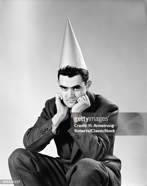 1950s DISGRUNTLED MAN WEARING DUNCE CAP LOOKING AT CAMERA