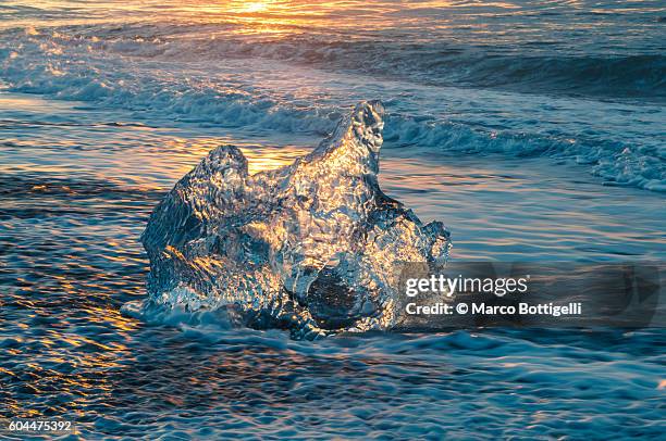 jokulsarlon glacier lagoon, iceland. sunlight reflections over a small black of ice on the shore. - gemengde signalen uitzenden stockfoto's en -beelden