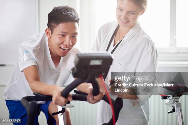 young man on exercise bike in university sports science department, young woman performing experiment and assessing performance - cultura orientale photos et images de collection