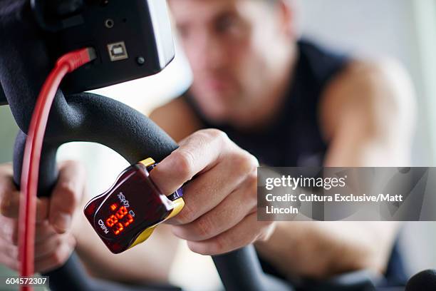 young man using exercise bike, wearing finger pulse oximeter on finger - the performance screening stockfoto's en -beelden