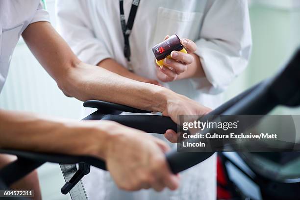 young man using exercise bike, young woman assessing his performance, mid section - cultura orientale photos et images de collection