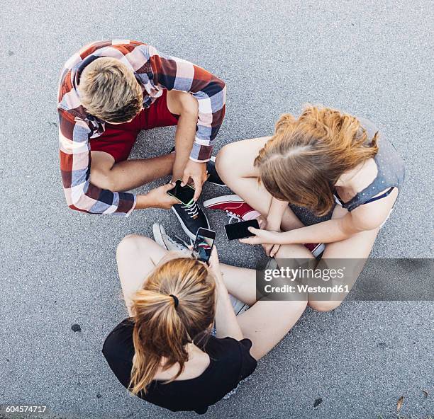 three teenagers sitting outdoors with smartphones - smartphones dangling stock pictures, royalty-free photos & images