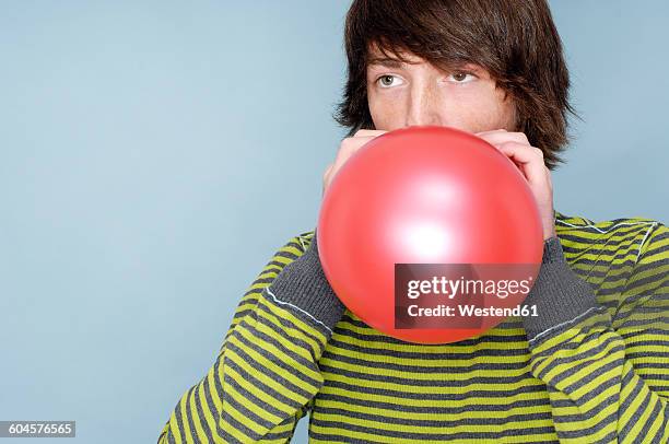 teenage boy blowing red balloon in front of blue background - blowing up balloon stock-fotos und bilder